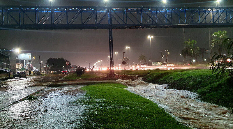 Uma forte chuva que atingiu Valparaíso de Goiás na noite desta quarta-feira, 4 de dezembro, expôs os desafios que esperam pelo prefeito eleito Marcus Vinícius. Apesar dos avanços recentes, a cidade ainda enfrenta uma infraestrutura precária, construída há mais de 30 anos e marcada pela falta de planejamento urbano, o que agrava os problemas durante as intensas chuvas. A tempestade provocou enxurradas de grande magnitude, arrastando veículos e alagando ruas e imóveis. Próximo à Câmara Municipal, um carro foi levado por alguns metros, perdendo o para-choque, que ficou jogado no gramado. A situação foi ainda mais crítica na BR-040, onde a marginal se transformou em um verdadeiro rio, colocando motoristas e pedestres em risco. No Atacadão Costa, um enorme alagamento se formou novamente, dificultando o trânsito e evidenciando a fragilidade da infraestrutura urbana. Em frente à Faculdade Anhanguera, o tráfego foi interrompido, criando sérios obstáculos para motoristas. Os bairros residenciais também foram severamente afetados. No setor de chácaras Ipiranga, as águas invadiram casas e apartamentos térreos do residencial Varandas IV. Moradores registraram cenas impactantes em que carros eram arrastados pela força da enxurrada, enquanto outros lutavam para conter a inundação dentro de suas residências. Essa situação em Valparaíso destaca a urgência de uma gestão que busque soluções estruturais para mitigar os efeitos das chuvas e evitar tragédias como a vivenciada nesta semana. Marcus Vinícius terá o desafio de reverter décadas de descaso e preparar a cidade para enfrentar eventos climáticos extremos com maior segurança. Cansada de ver cenas recorrentes de alagamentos, a população aguarda ações efetivas para transformar a realidade de Valparaíso de Goiás.